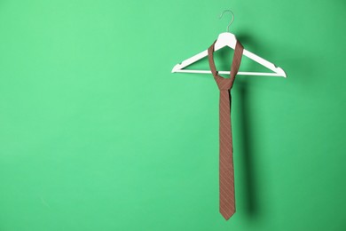 Hanger with brown striped tie on green background. Space for text
