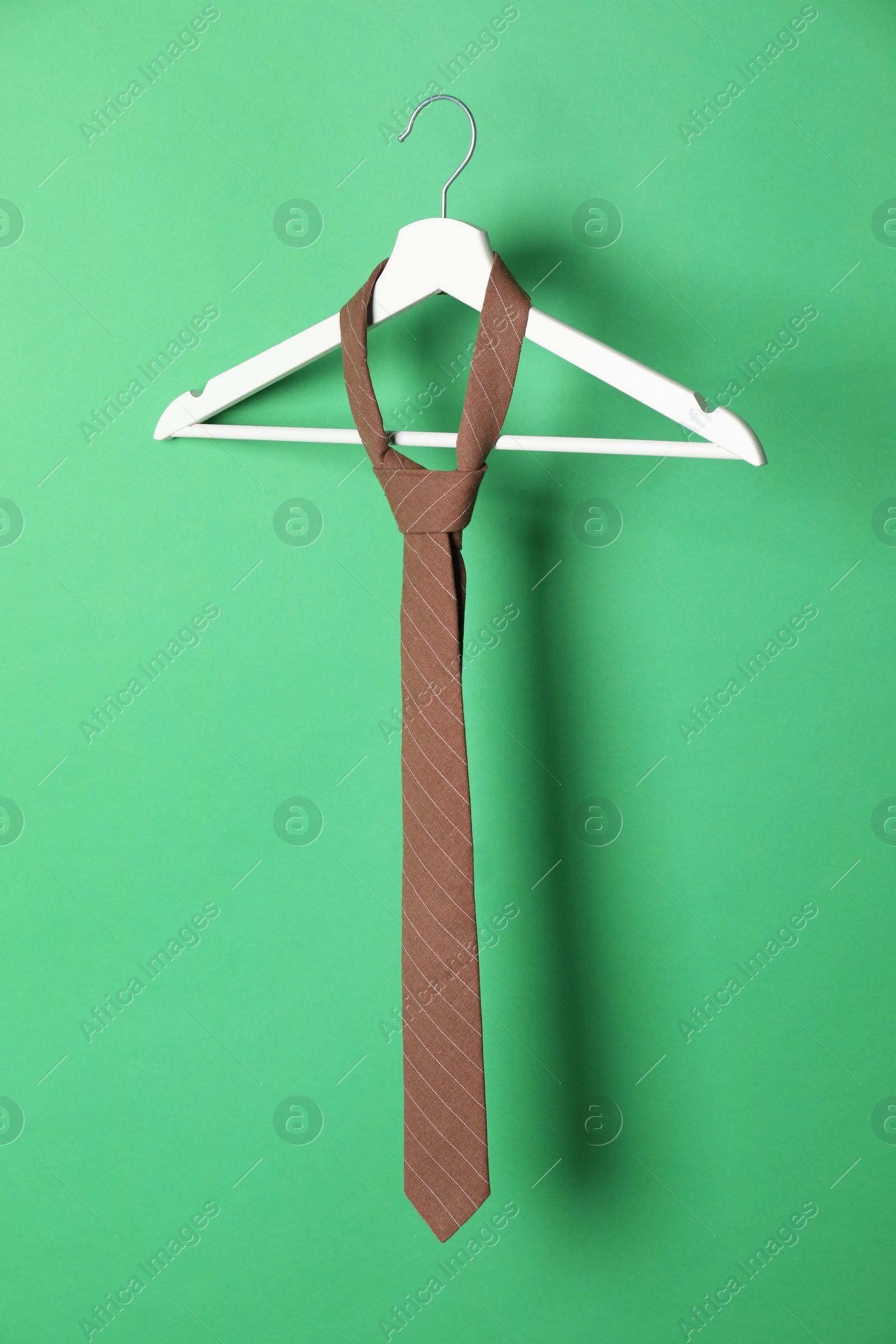 Photo of Hanger with brown striped tie on green background