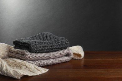 Photo of Knitted scarfs on wooden table against gray background, space for text