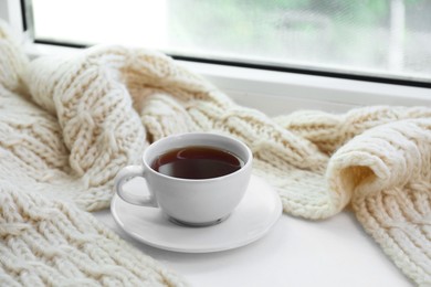 Photo of Beige knitted scarf and tea on windowsill