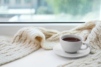 Beige knitted scarf and tea on windowsill