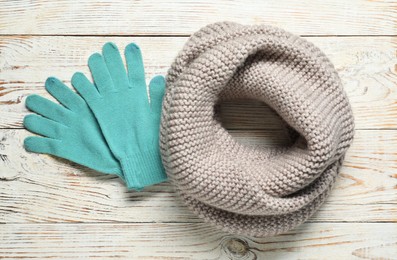 Gray knitted scarf and gloves on light wooden table, flat lay