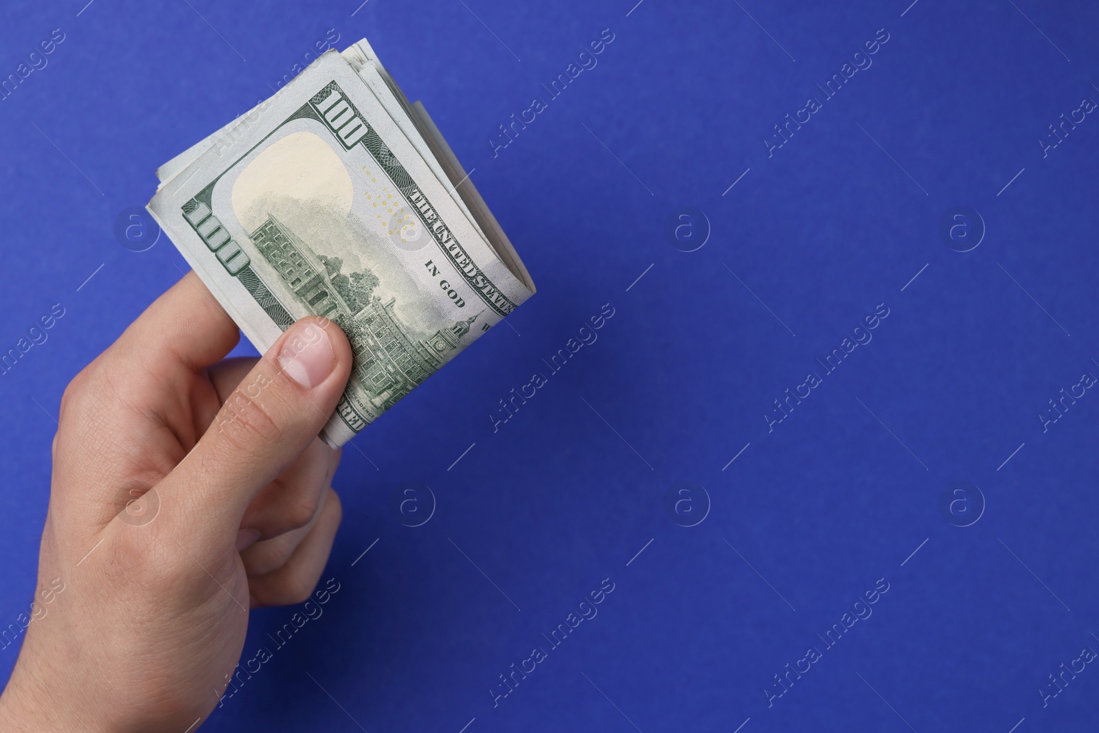 Photo of Money exchange. Man holding dollar banknotes on blue background, top view. Space for text