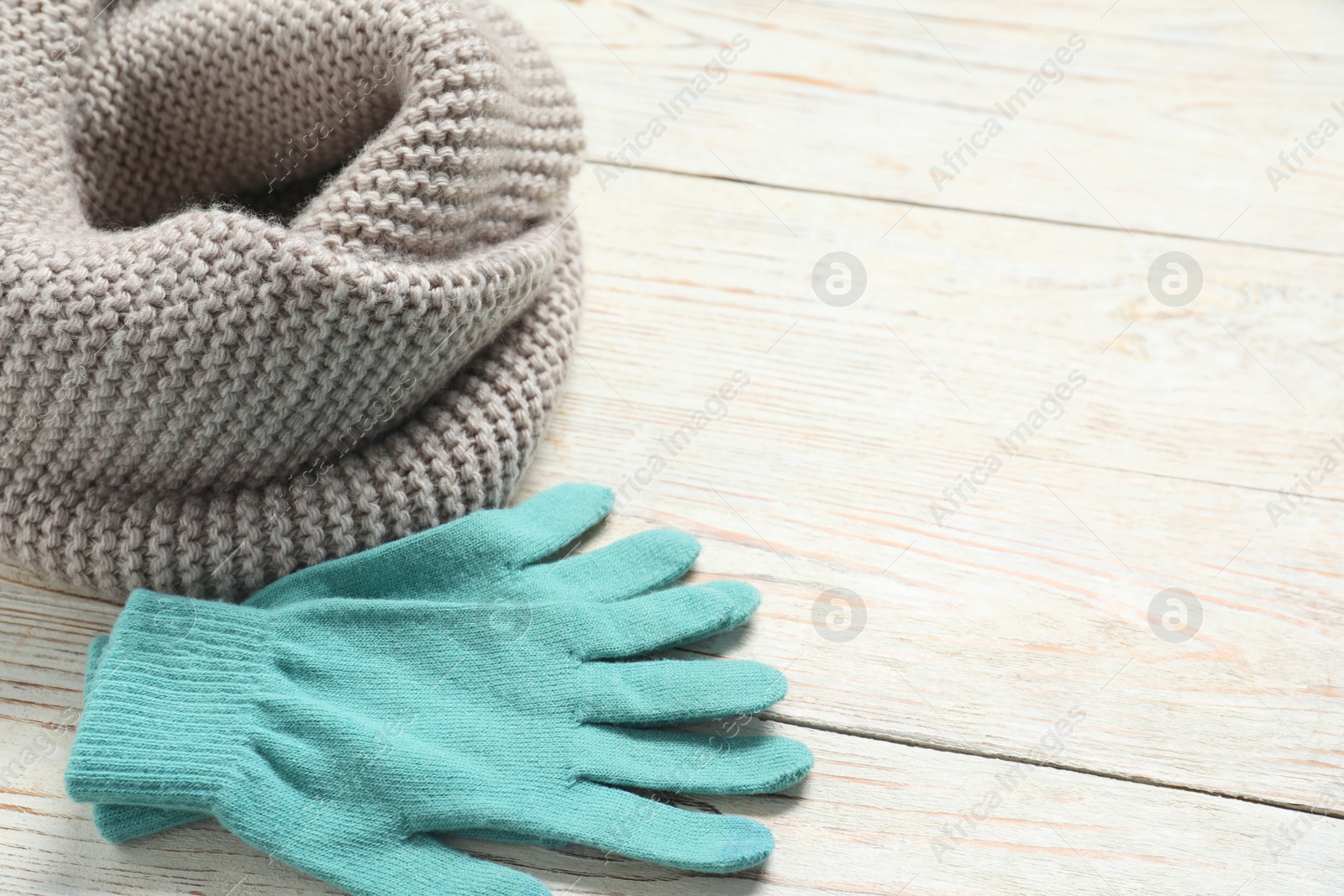 Photo of Gray knitted scarf and gloves on light wooden table, closeup. Space for text