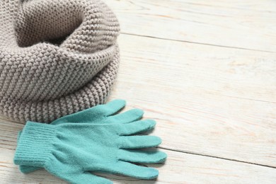 Gray knitted scarf and gloves on light wooden table, closeup. Space for text
