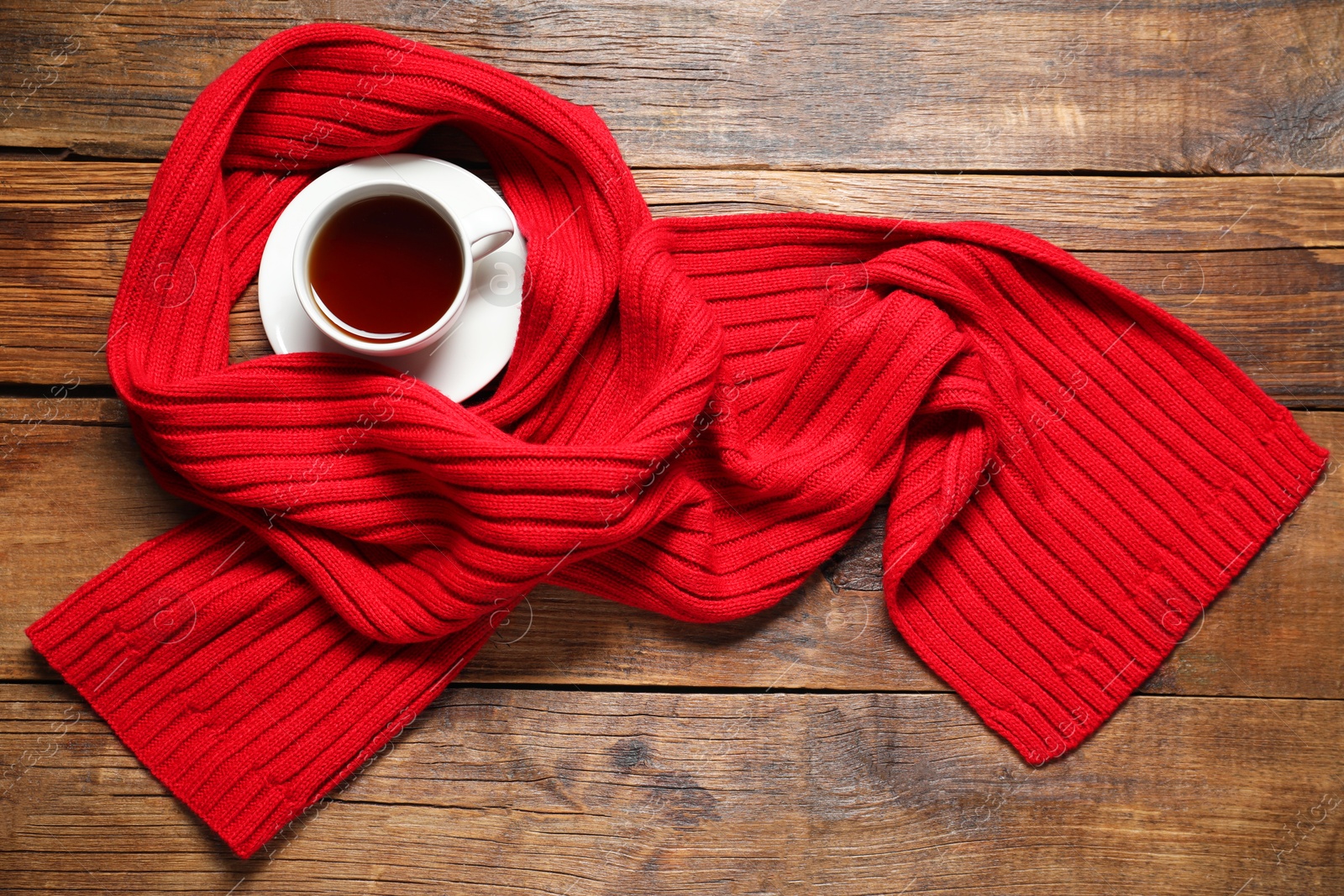 Photo of Red knitted scarf and tea on wooden table, top view