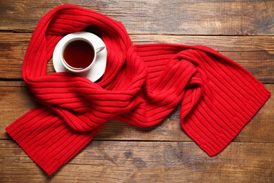 Photo of Red knitted scarf and tea on wooden table, top view