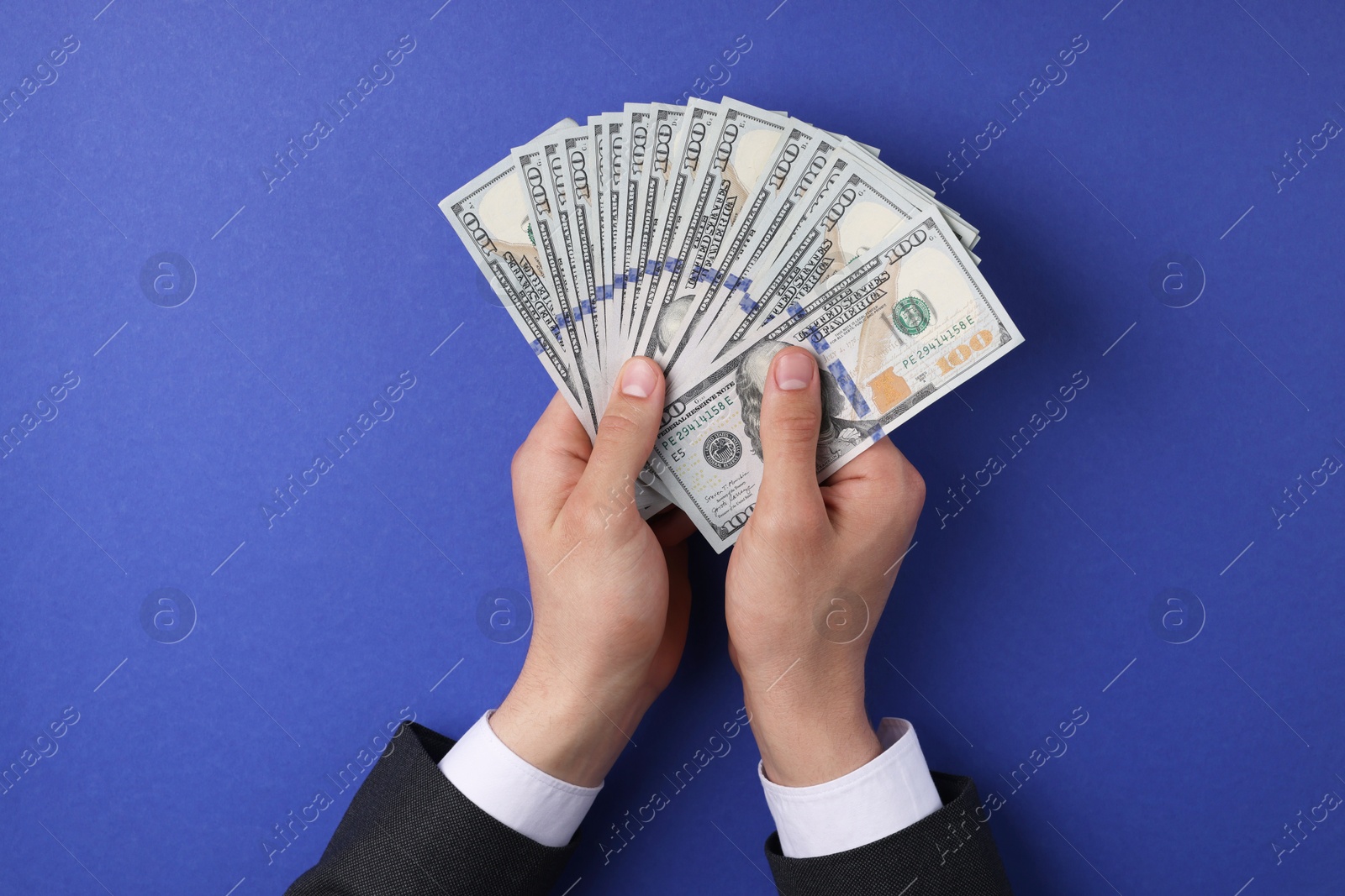 Photo of Money exchange. Man holding dollar banknotes on blue background, top view