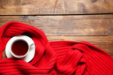 Photo of Red knitted scarf and tea on wooden table, top view. Space for text