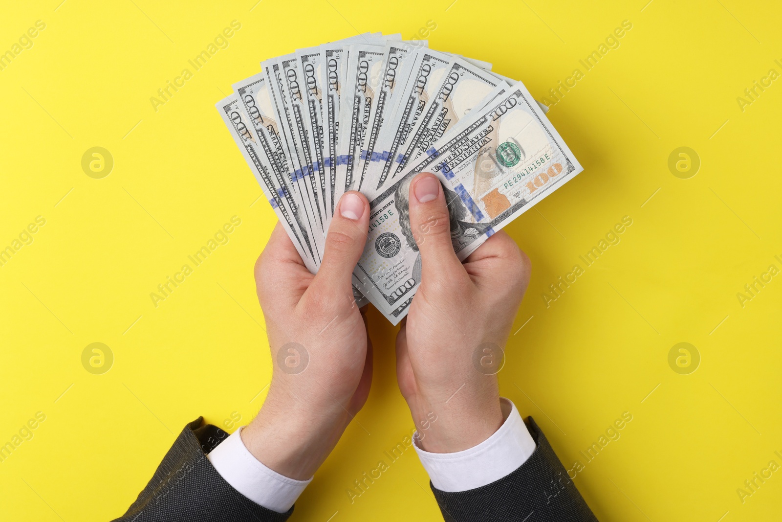 Photo of Money exchange. Man holding dollar banknotes on yellow background, top view