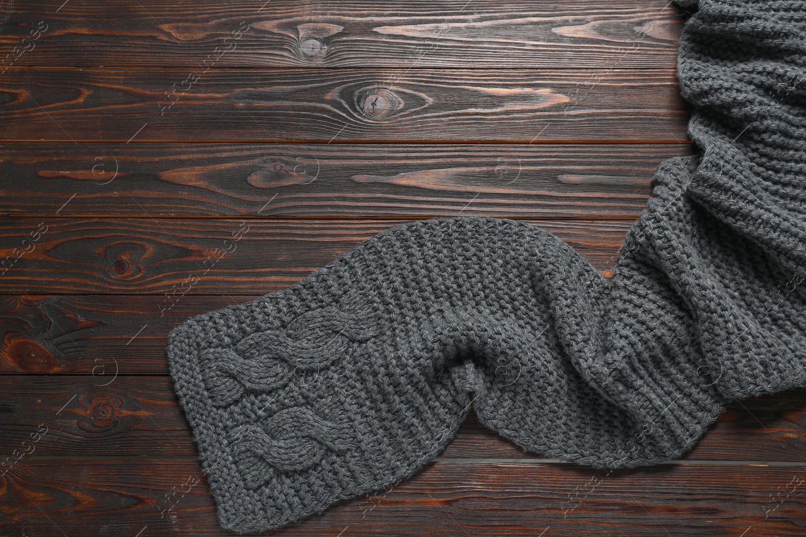 Photo of Gray knitted scarf on wooden table, top view. Space for text