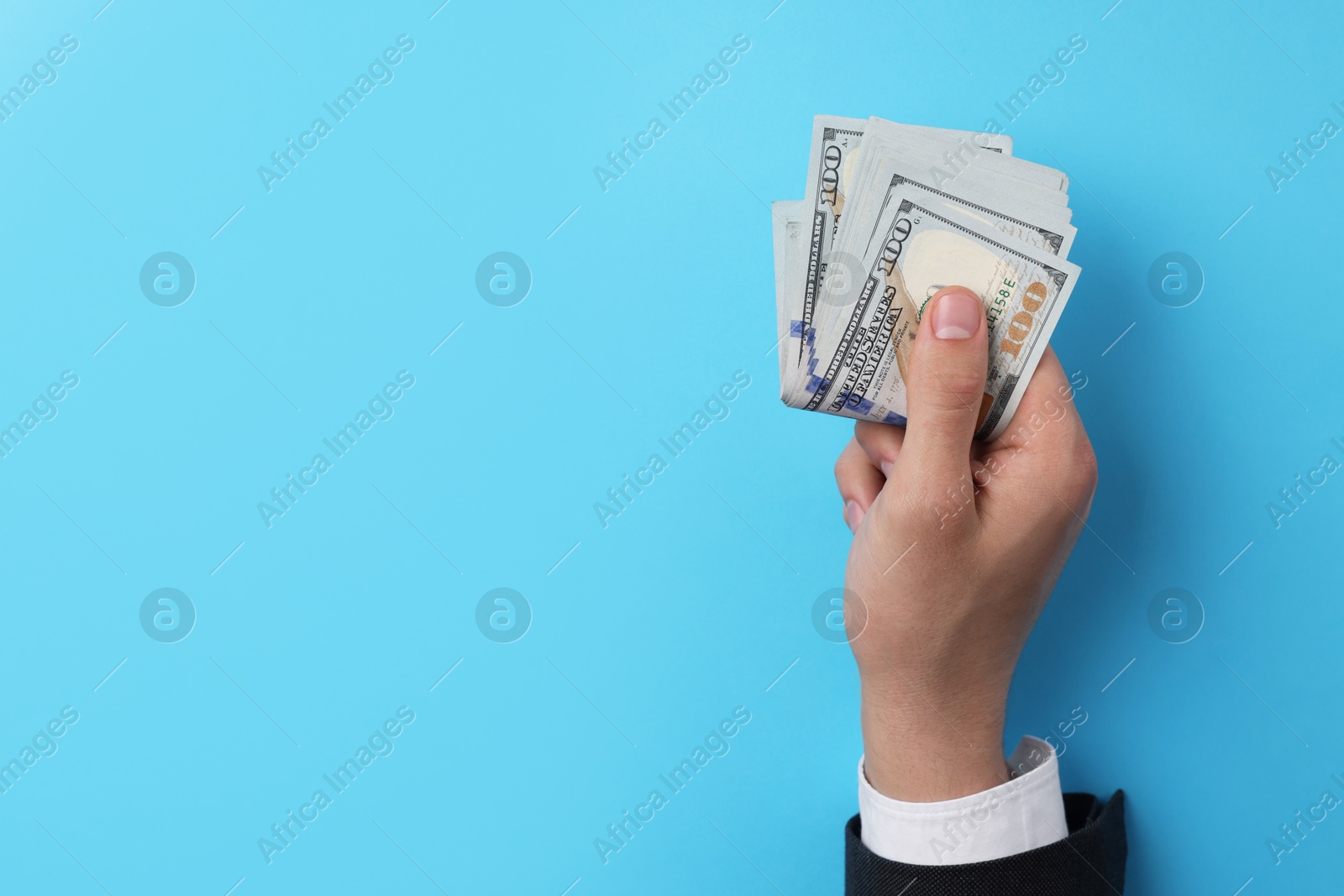 Photo of Money exchange. Man holding dollar banknotes on light blue background, top view. Space for text