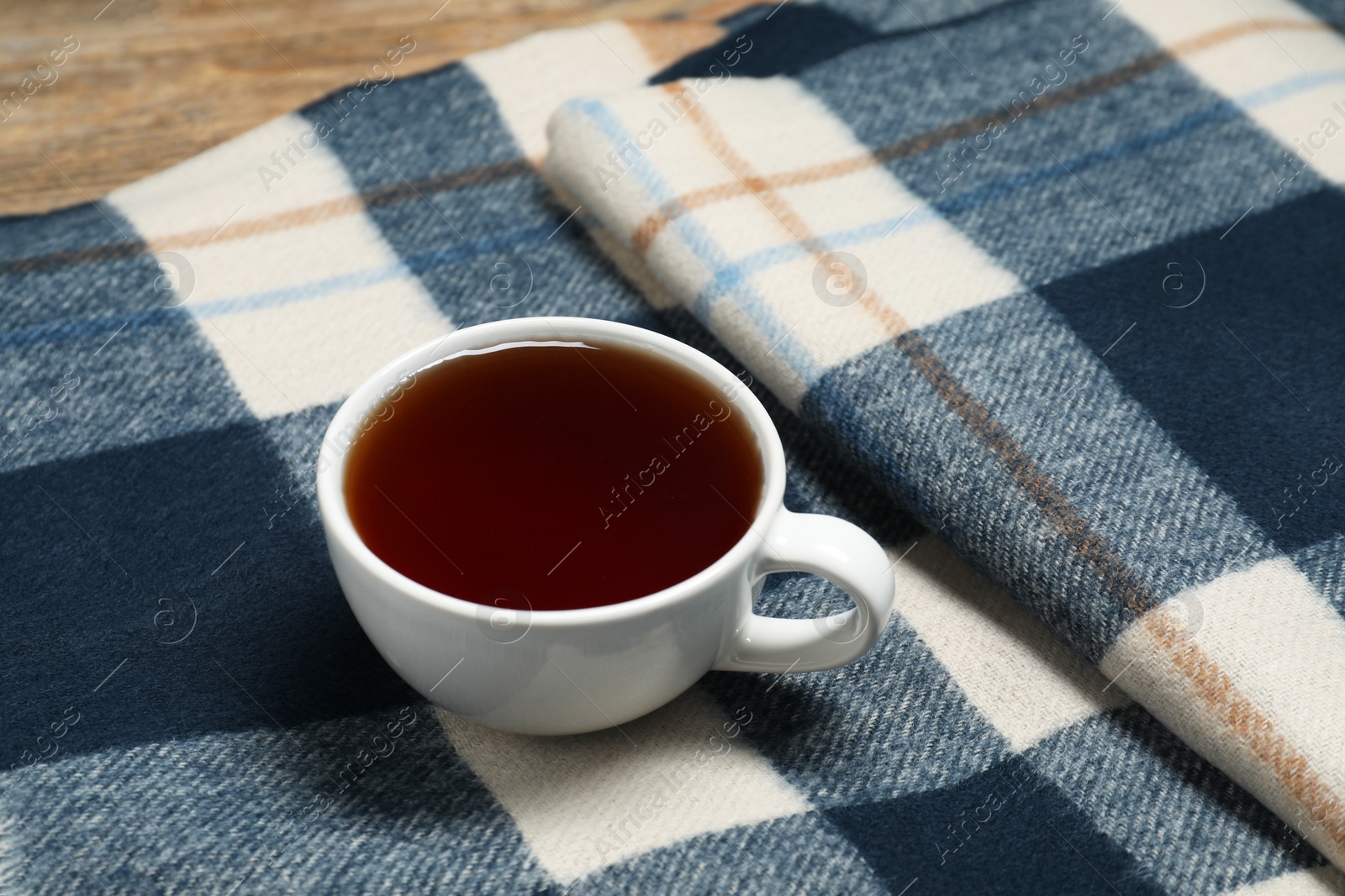 Photo of Soft checkered scarf and tea on table, closeup