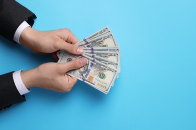 Photo of Money exchange. Man holding dollar banknotes on light blue background, top view