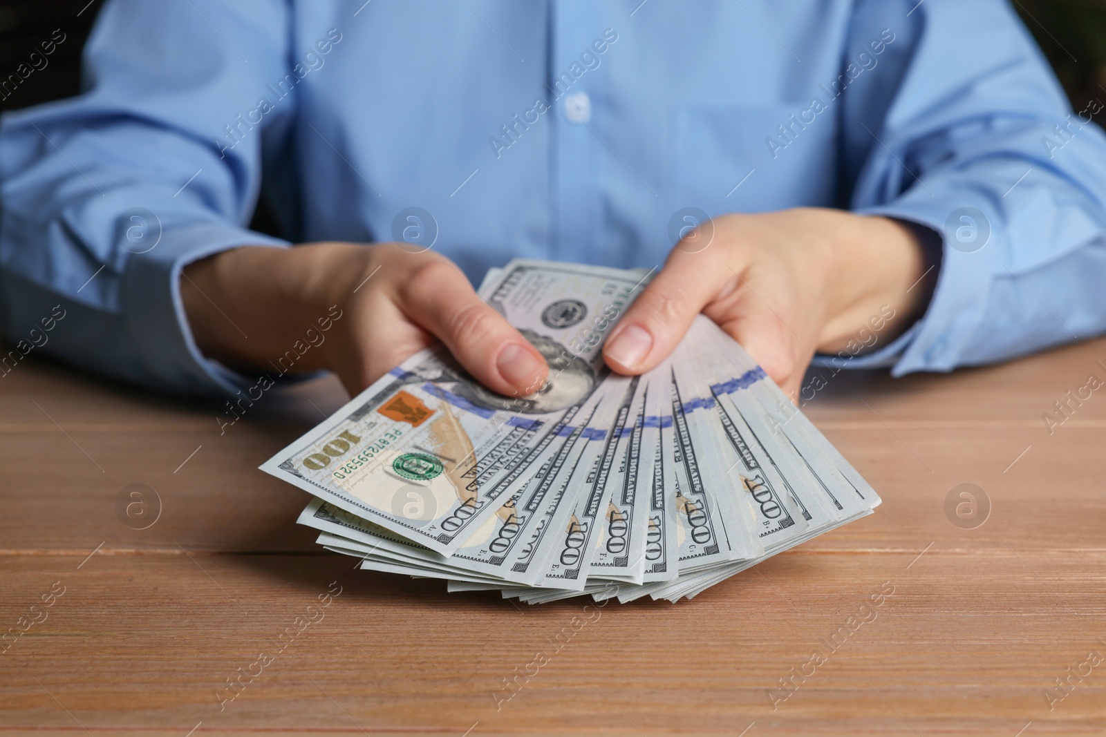 Photo of Money exchange. Woman holding dollar banknotes at wooden table, closeup