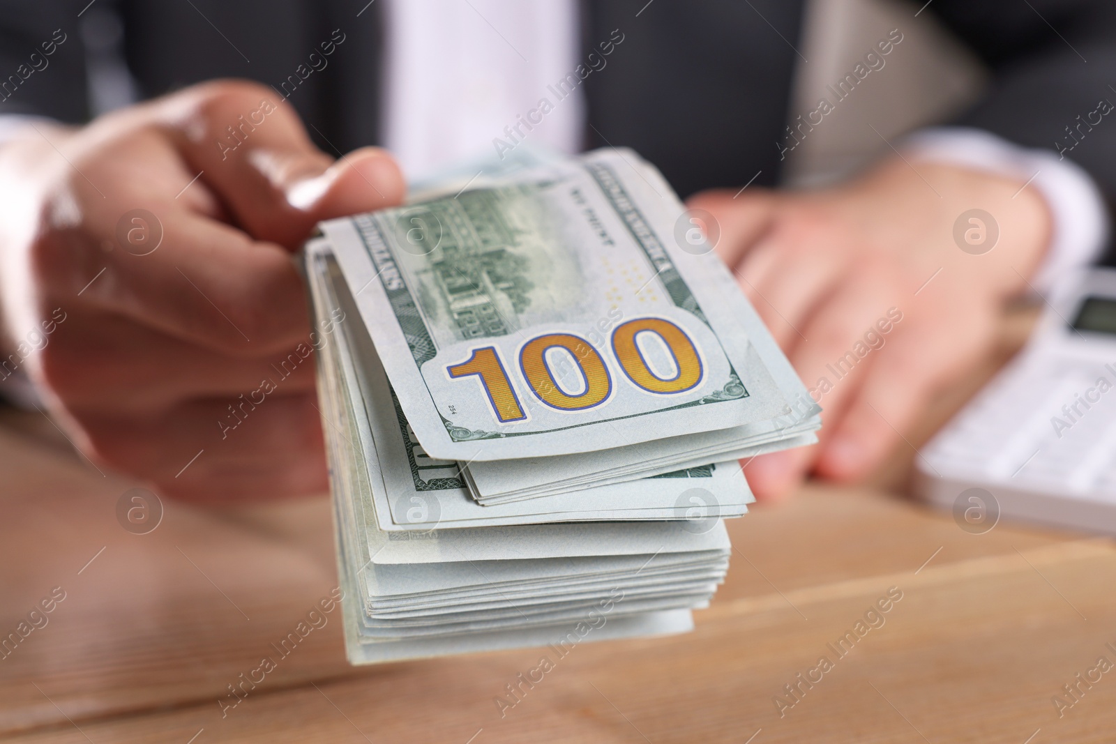 Photo of Money exchange. Man holding dollar banknotes at wooden table, closeup