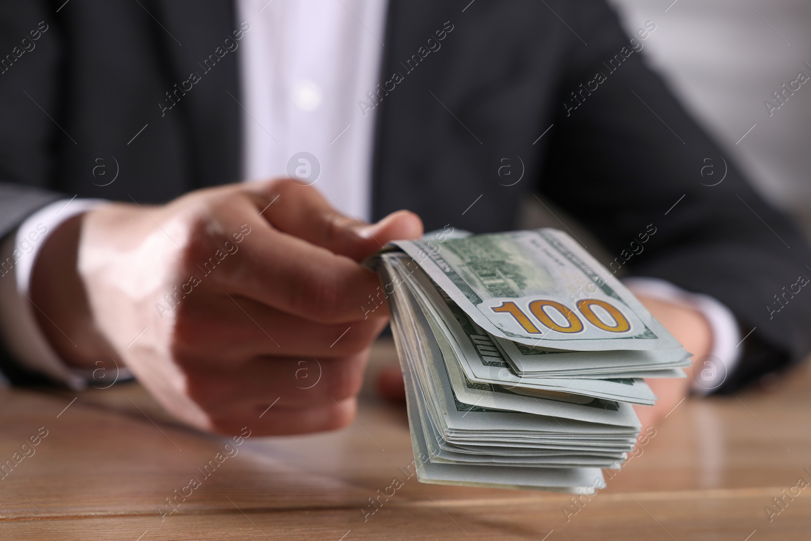 Photo of Money exchange. Man holding dollar banknotes at wooden table, closeup