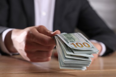 Money exchange. Man holding dollar banknotes at wooden table, closeup