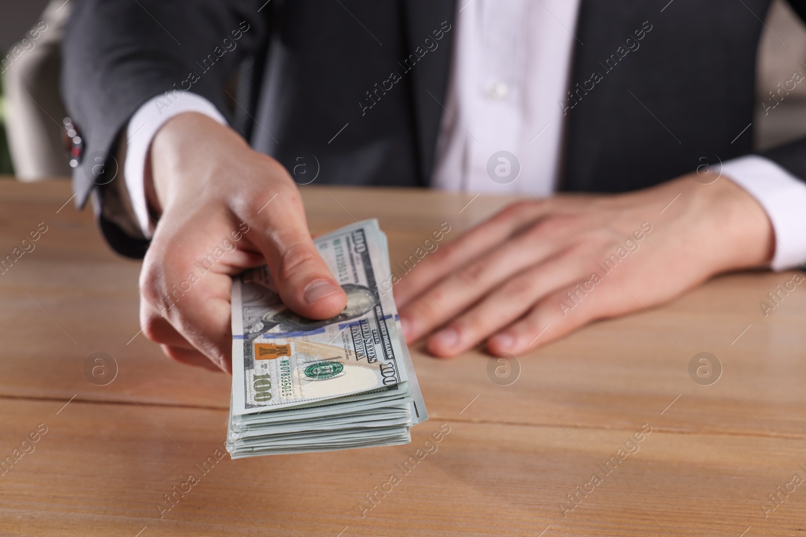 Photo of Money exchange. Man holding dollar banknotes at wooden table, closeup