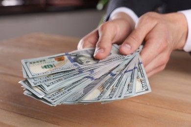 Photo of Money exchange. Man counting dollar banknotes at wooden table, closeup