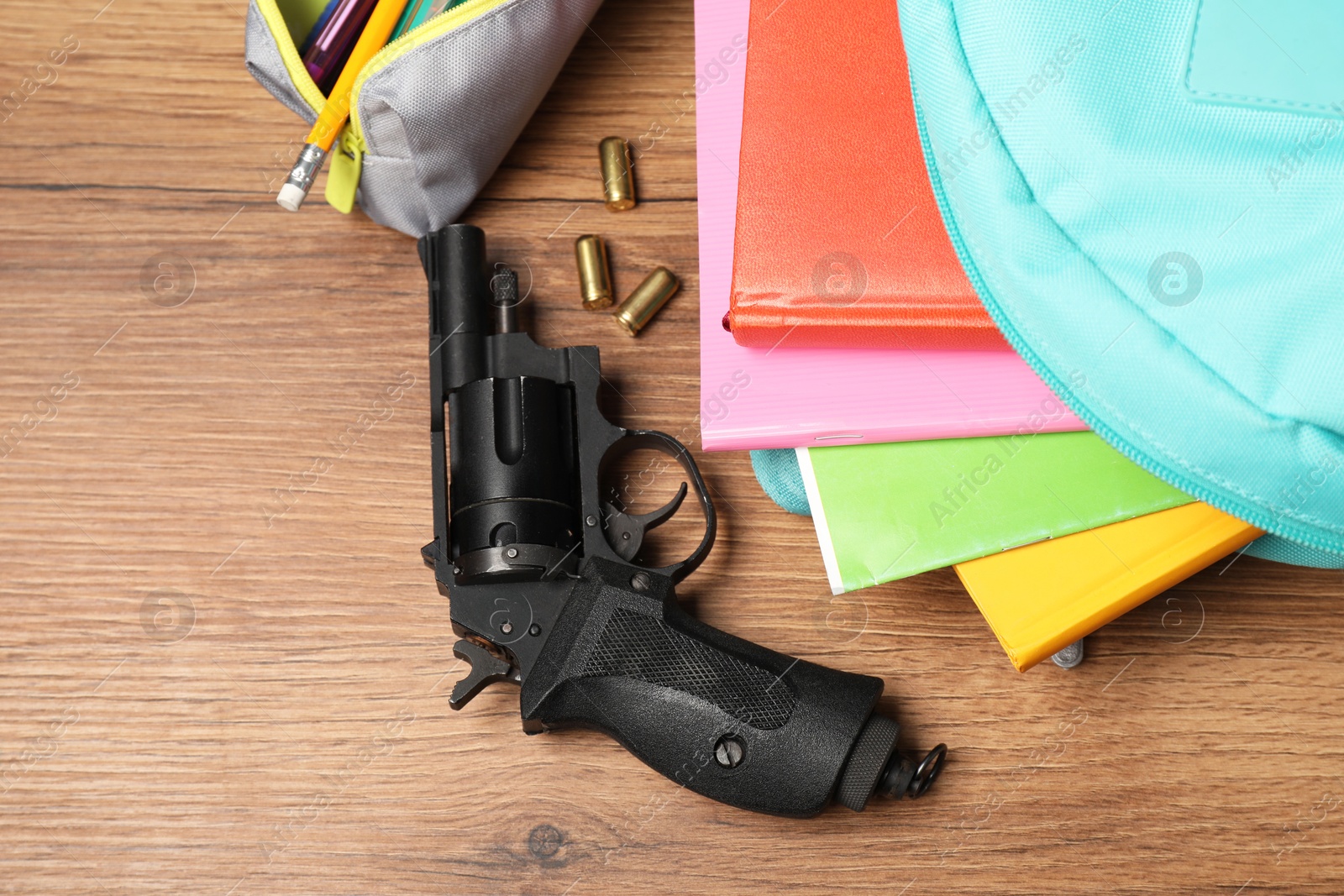 Photo of Gun, bullets and school stationery on wooden table, flat lay