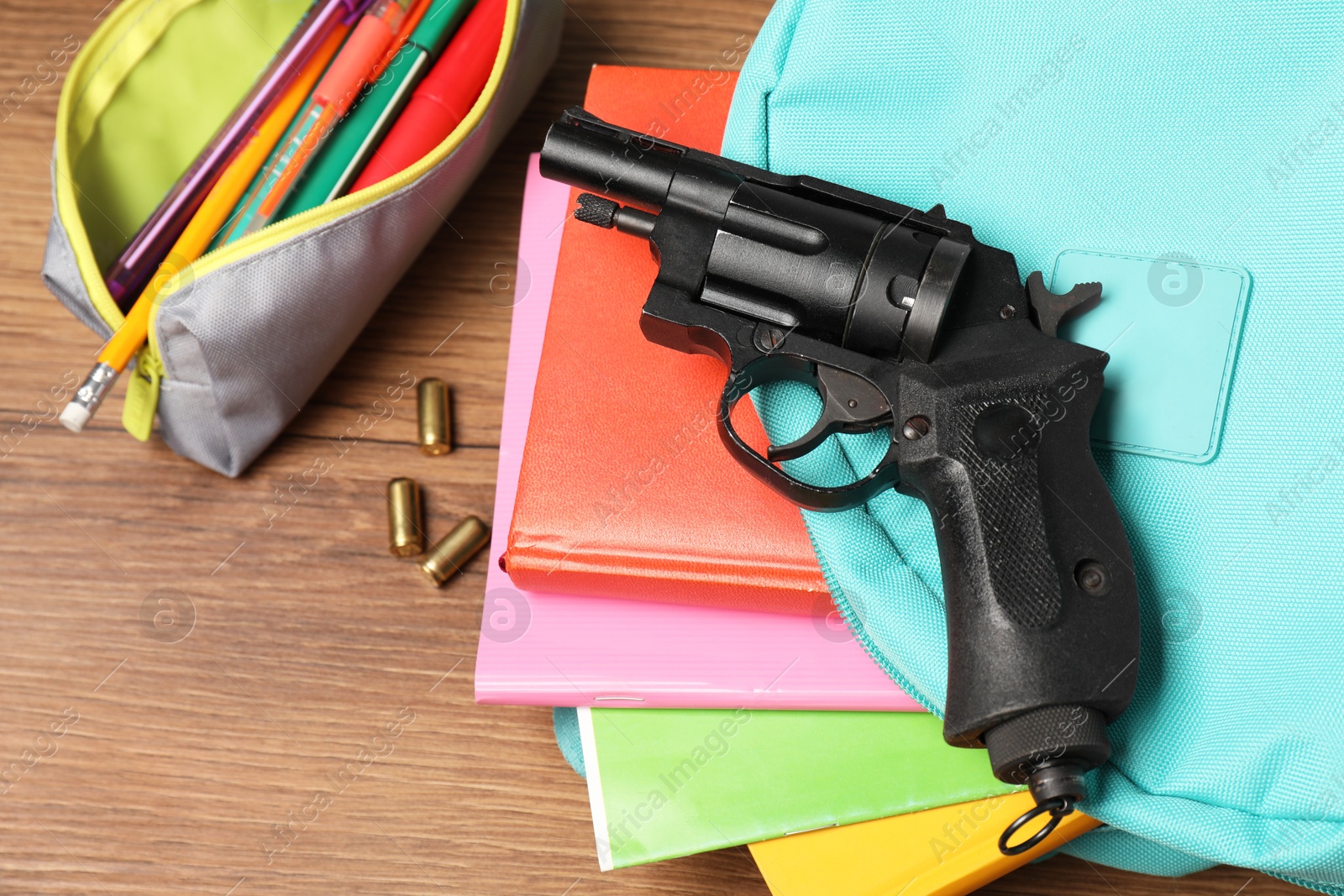 Photo of Gun, bullets and school stationery on wooden table, flat lay