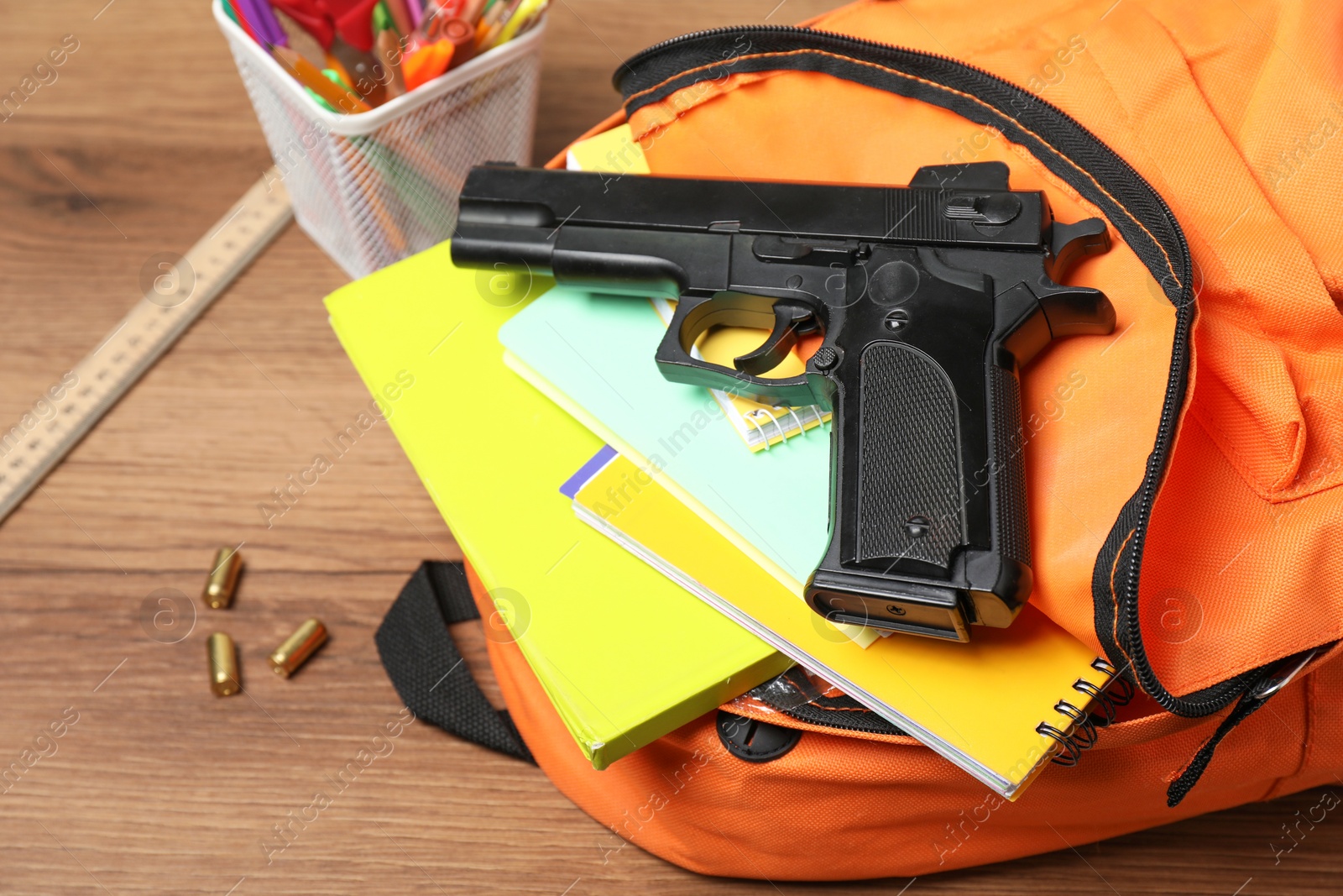 Photo of Gun, bullets and school stationery on wooden table , closeup