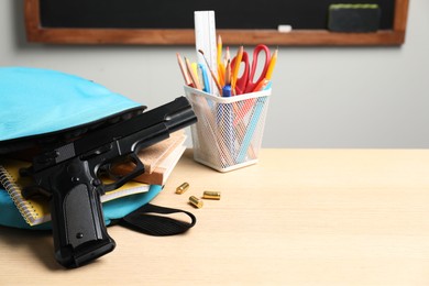 Photo of Gun, bullets and school stationery on wooden table near blackboard indoors, space for text