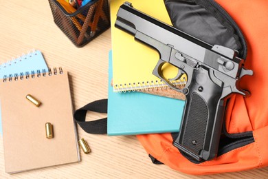 Photo of Gun, bullets and school stationery on wooden table, flat lay