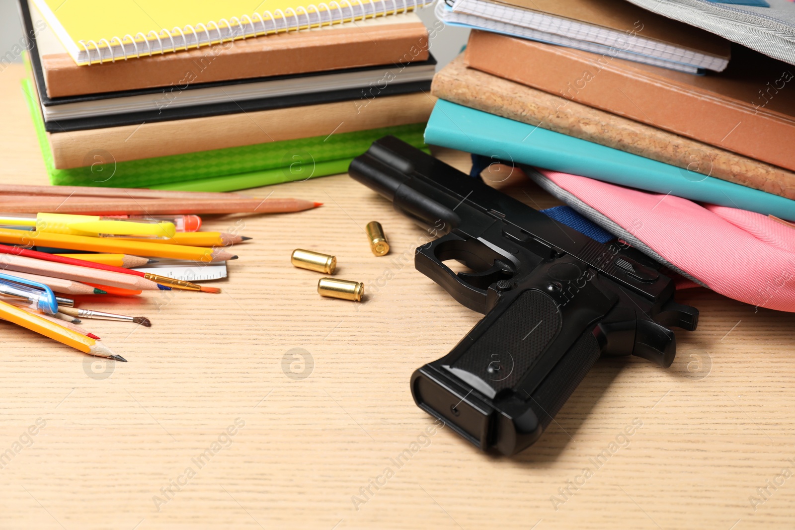 Photo of Gun, bullets and school stationery on wooden table