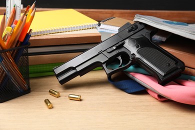 Photo of Gun, bullets and school stationery on wooden table