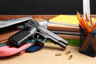 Photo of Gun, bullets and school stationery on wooden table