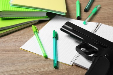 Photo of Gun and school stationery on wooden table, closeup