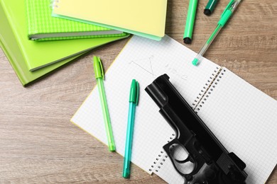 Photo of Gun and school stationery on wooden table, flat lay