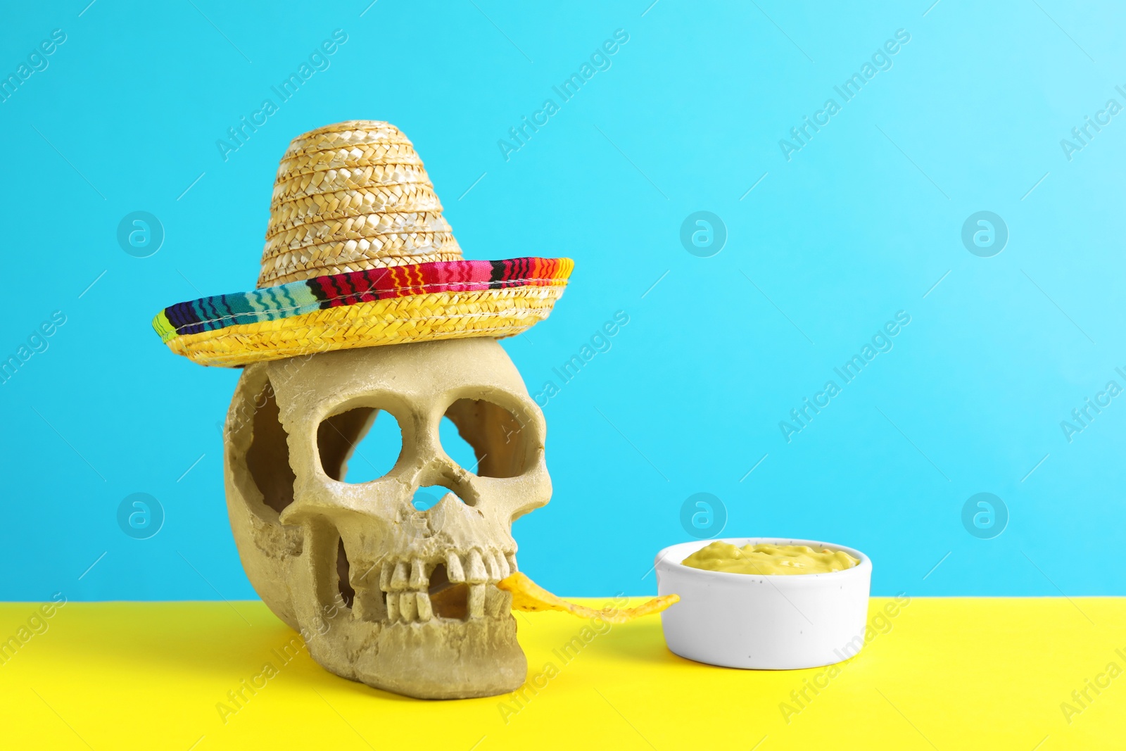 Photo of Human scull with Mexican sombrero hat, nachos chip and guacamole on color background. Space for text