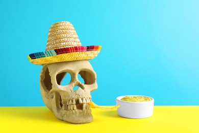 Photo of Human scull with Mexican sombrero hat, nachos chip and guacamole on color background. Space for text