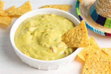 Delicious guacamole with nachos chips on white wooden table, closeup