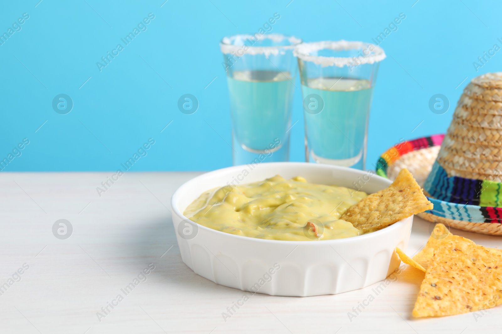 Photo of Mexican sombrero hat, nachos chips, tequila and guacamole on white wooden table