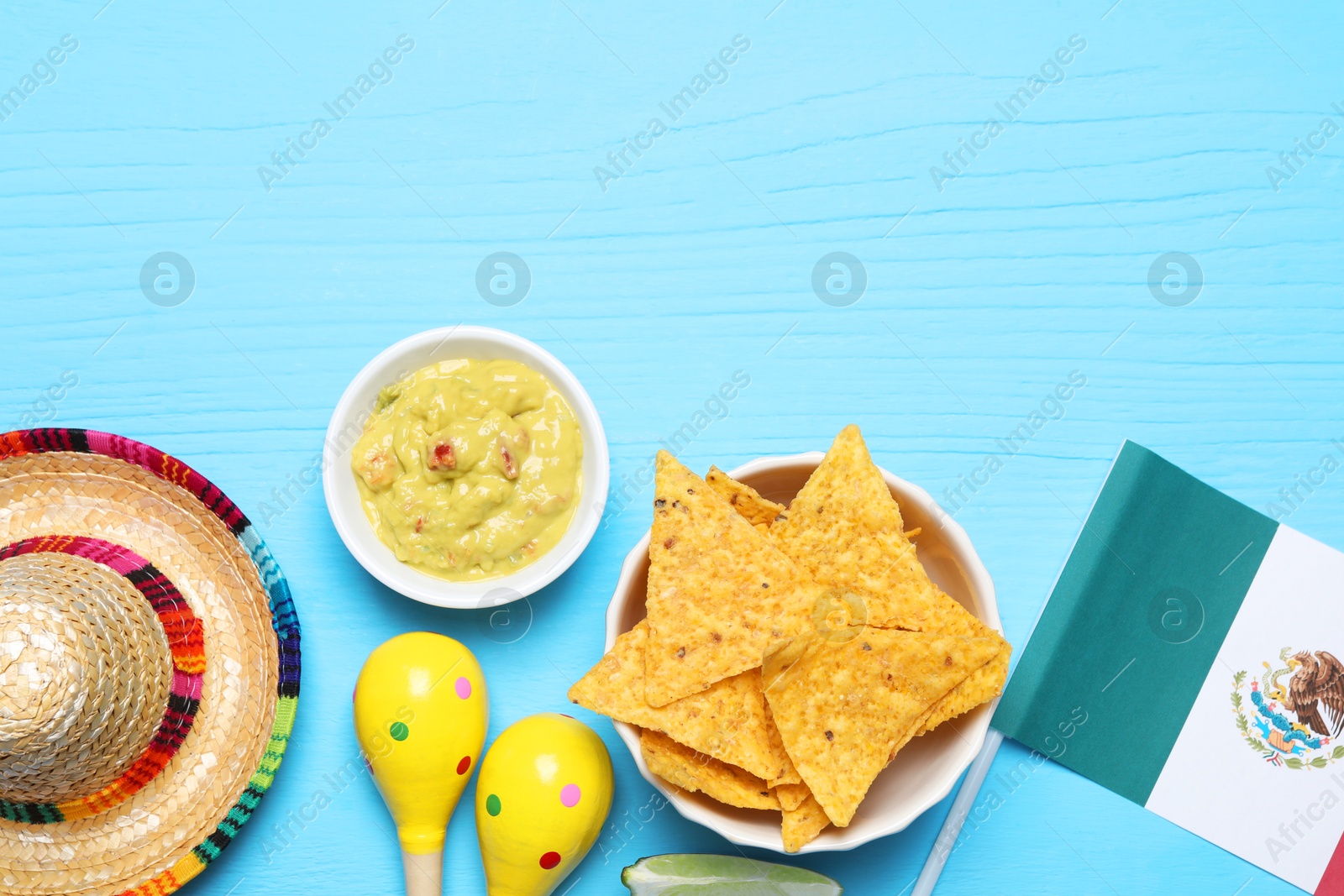 Photo of Mexican flag, sombrero hat, maracas, nachos chips and guacamole on light blue wooden table, flat lay. Space for text