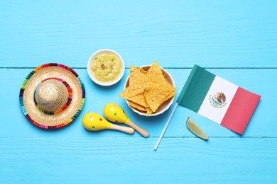 Mexican flag, sombrero hat, maracas, nachos chips and guacamole on light blue wooden table, flat lay