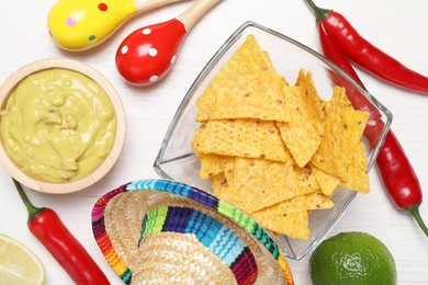 Photo of Delicious guacamole with nachos chips, Mexican sombrero hat and maracas on white wooden table, flat lay