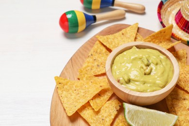 Photo of Delicious guacamole with nachos chips, Mexican sombrero hat and maracas on white wooden table, closeup. Space for text