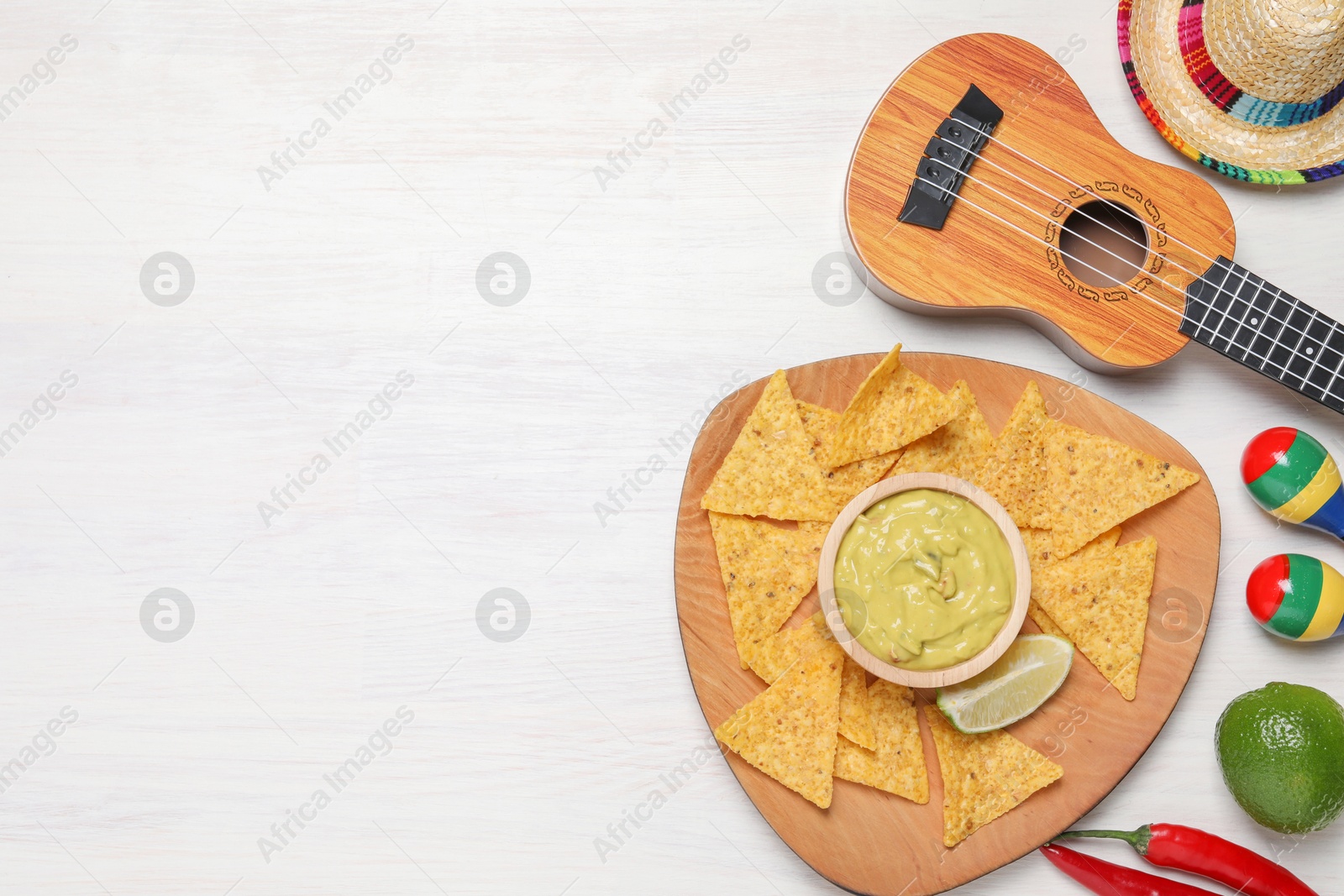 Photo of Delicious guacamole with nachos chips, Mexican sombrero hat, ukulele and maracas on white wooden table, flat lay. Space for text