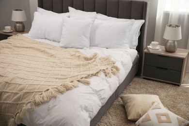 Many soft white pillows and knitted blanket on bed indoors