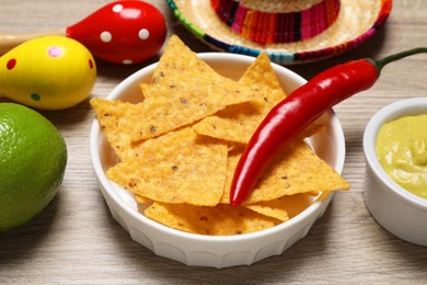 Photo of Nachos chips, chili pepper, maracas, lime and Mexican sombrero hat on wooden table, closeup