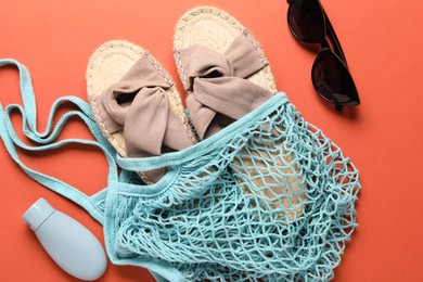 Photo of String bag, sunglasses, slippers and cosmetic product on coral background, top view