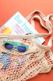 String bag, sunglasses and magazine on coral background, top view