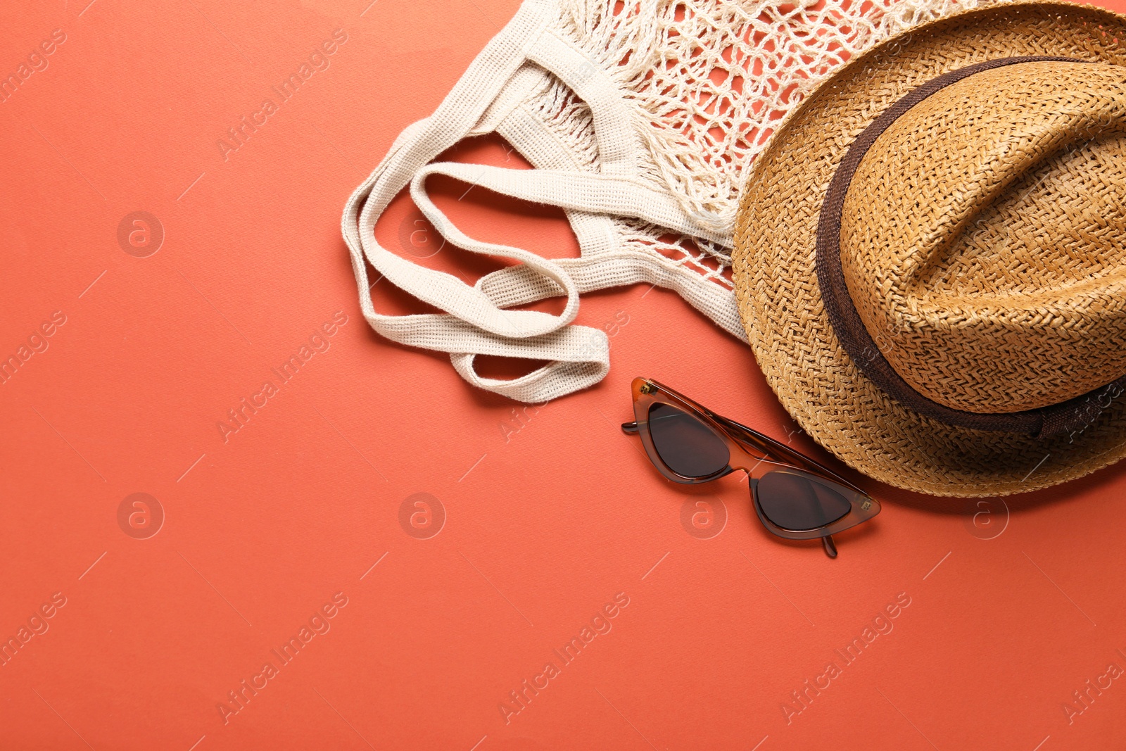 Photo of String bag, sunglasses and hat on coral background, top view. Space for text