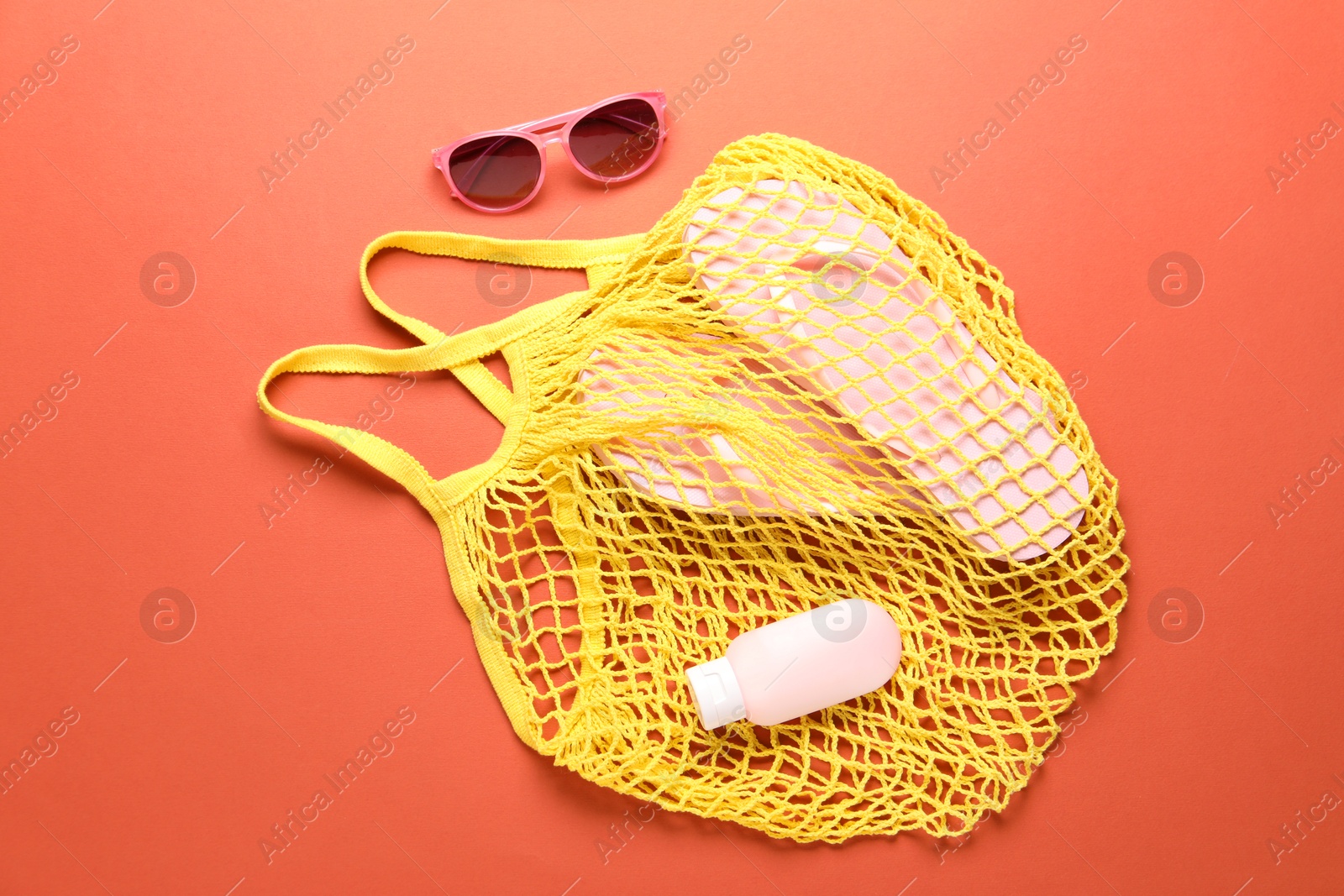 Photo of String bag, sunglasses, cosmetic product and slippers on coral background, top view