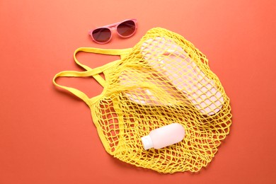 Photo of String bag, sunglasses, cosmetic product and slippers on coral background, top view